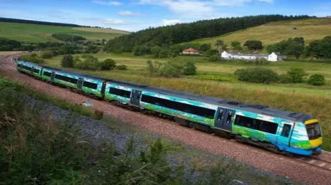 A colourful blue, green and yellow train speeds through the Scottish Borders countryside
