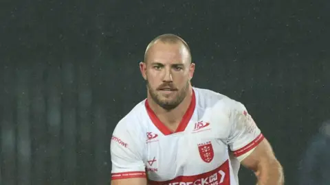 Karl Lawton carrying the ball in both hands but slightly towards his left-hand side playing for Hull KR