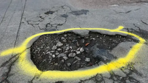 A large pothole is ringed in yellow luminescent spray paint