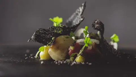 Moor Hall Holstein Friesian, barbecued celeriac, mustard and shallot artfully arranged on a black plate