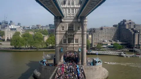 PA Media A aerial of colourfully dressing marathon competitors crossing Tower Bridge. 