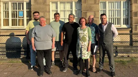 LDRS Image shows several New Ferry residents standing outside the town hall. There are six men and female councillor Jo Bird. 