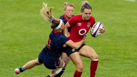 England's Ellie Kildunne in action during the Women's Rugby International match between England Women and USA Women at Sandy Park on September 3, 2022 in Exeter, England. She is being tackled by two USA players.