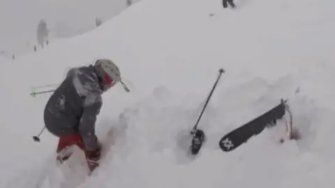 A rescuer is rescuing a skier that is under the snow.