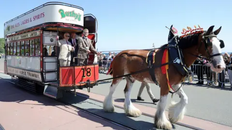 PA Media The King on a double decker horse tram pulled by a brown horse.