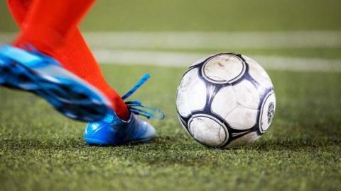 A stock image of a footballer in blue football boots and red socks about to kick a ball. They are only photographed from the ankles