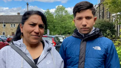 A woman in a grey hooded top and teenage boy in a black and blue hooded jacket.