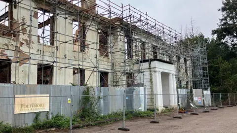 The facade of a mansion house, burnt, and surrounding by scaffolding.
