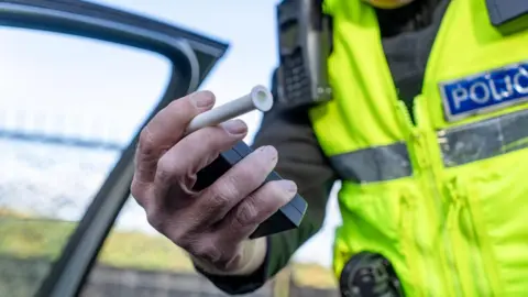 Getty Images A man in an yellow reflective jacket holding out a black box with a white tube coming out of it