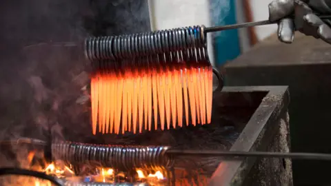 Whiteley & Sons Dozens of red-hot scissors are removed from a forge.