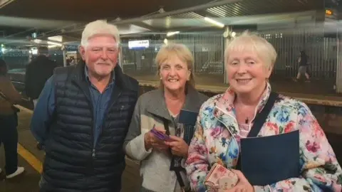 Three people standing on a train station platform