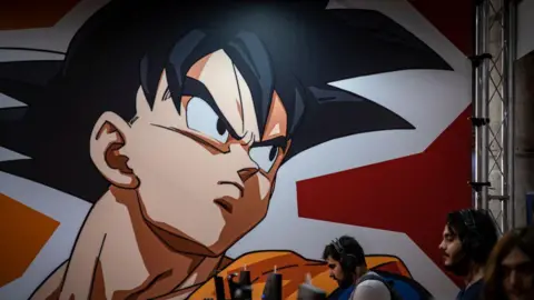 A graphic from the Dragon Ball Z comic is seen displayed on a wall above several people on computers