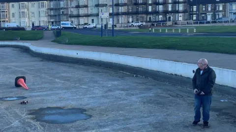 A club member racing a radio controlled car in the empty lake. There is an overturned orange cone.