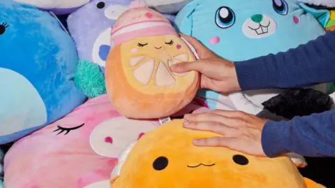 A pile of Squishmallows with one being held in a hand.