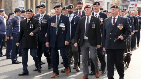 Eddie Mitchell Veterans wearing medals and berets marching along a street