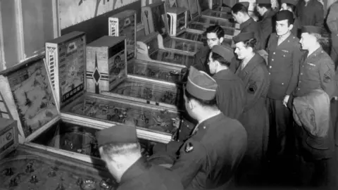 Getty Images A black and white photo of American soldiers playing pin-ball at Rainbow Corner, the American Red Cross Club for American troops in London