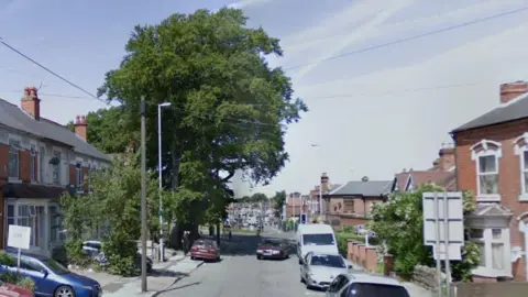 Springfield Road in Kings Heath with houses on both sides, parked cars and lampposts and a roundabout further along the road near a large tree.