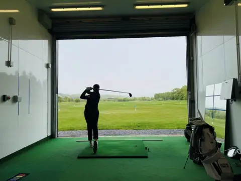 Robyn Fowlie after hitting a golf ball on a driving range, she is silhouetted, with the club swung behind her head.