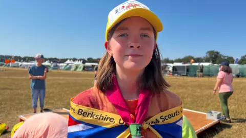 A girl wearing Scout uniform stood outside on a sunny day