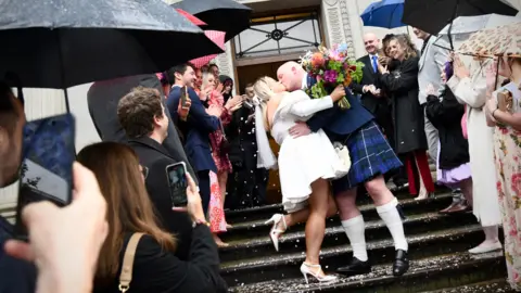 Emma Lynch / BBC Thomas Mackintosh and Paige Evans kiss on the steps of the town hall