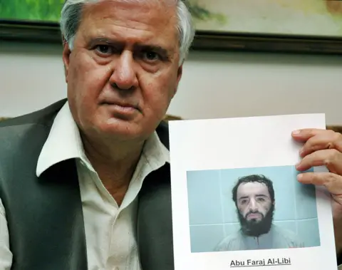 AFP via Getty Images Pakistan's interior minister at the time Aftab Ahmed Khan Sherpao looks at the camera while holding a printed image of a mugshot of Abu Faraj al-Libi, in Islamabad in 2005.
