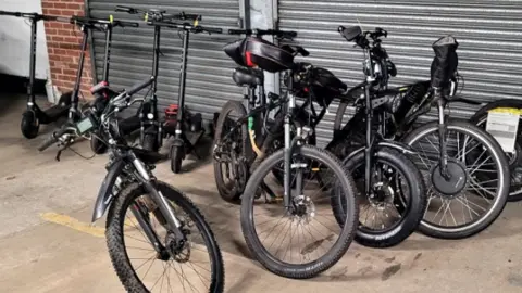 Nottinghamshire Police A number of black e-scooters and e-bikes in front of a metal shuttered entrance