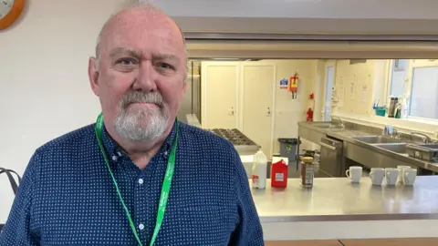 John Weston from Bollington Town Council is a largely bald man with a grey goatee beard. He wears a dark blue shirt with small light blue dots.