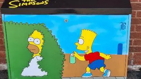 BBC A black street cabinet has been painted with an image of cartoon characters Bart and Homer Simpson.