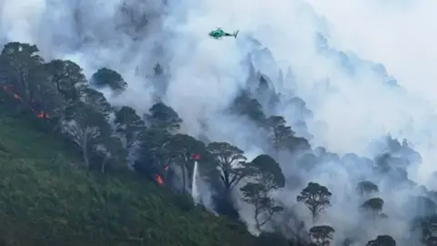 A helicopter waterbombs a large wildfire 