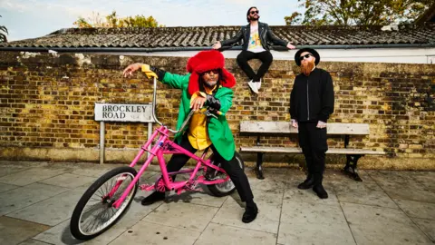 Dean Chalkley Benji Webbe on a pink bike. The other members of Skindred are behind him