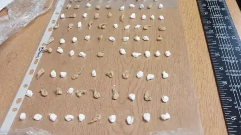 West Midlands Police Rows of small white packages on a wooden table with a black ruler alongside.