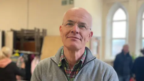 Giles Knight wearing a checked shirt and fleece, in the church