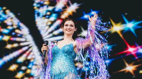 Luke Brennan/Getty Images Sophie Ellis-Bextor waving to the crowd with flashing lights behind her. 