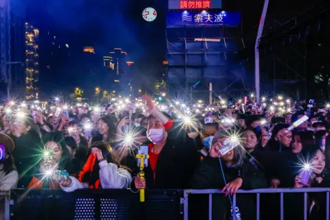 Daniel Ceng/Anadolu via Getty Images Orang-orang melambaikan senter ponsel pintar mereka saat perayaan hitung mundur Malam Tahun Baru, saat pulau itu bersiap menyambut tahun 2025, di luar Taipei 101, di Taipei, Taiwan, pada 31 Desember 2024.