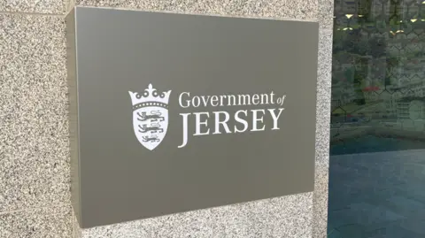 A picture of the from the front of the Government of Jersey building. There is a small sign which reads Government of Jersey in white.