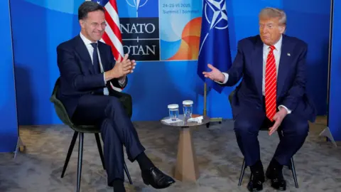 Mark Rutte and Donald Trump smile at a news conference, they are say in front of USA and Nato flags.