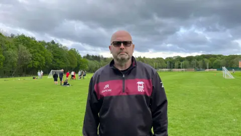 bbc Jason Rooney standing in  front of a football pitch