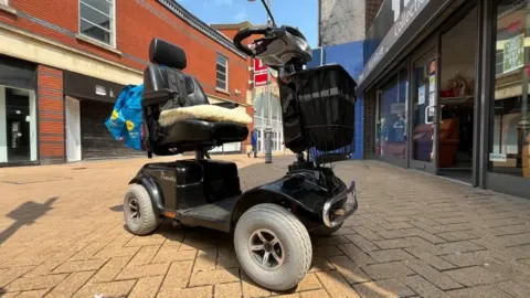 A view of a mobility scooter owned by a member of the public, with Idlewells Shopping Centre in the background.