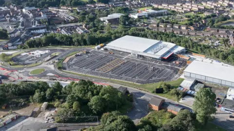 An aerial view of the new site, which has a large car park and a big white building, nestled among houses.