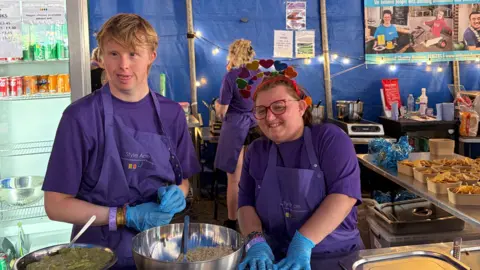 Style Acre Two Style Acre volunteers preparing food at Truck Festival. There are banners for Chill and Nachos and Cheese on Toast behind him.
