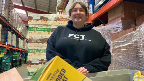 Bethany Willcox stands in a warehouse full of food products.