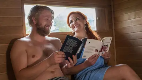 Getty Images Finnish authors Harri Hertell (L) and Katariina Vuorinen, both wearing only towels, smile and hold books as they give a reading in a mobile sauna - file photo