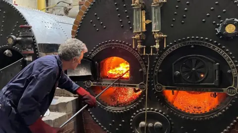 A view of a volunteer stoking a fire in one of the boiler room's boilers.