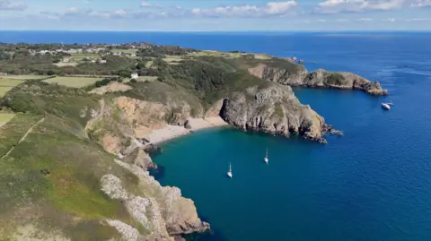 BBC A birds-eye view of Sark. To the left is the land and on the right is the sea with a few boats.