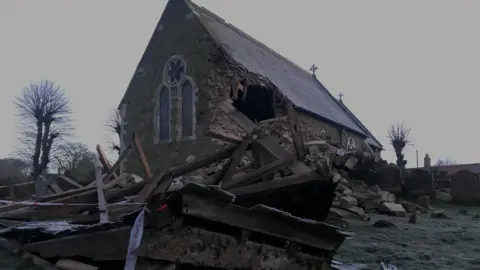 Harry Parkhill/ BBC Rubble and debris lie on a frosty graveyard floor in front of a church in the bakground. There's a large hole in the corner of the church with beams and bricks splling out of the hole