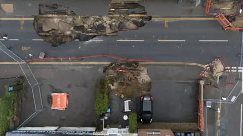 PA Media A view of the sinkholes from above with a car on a driveway very close to the edge of the smaller, second sinkhole.