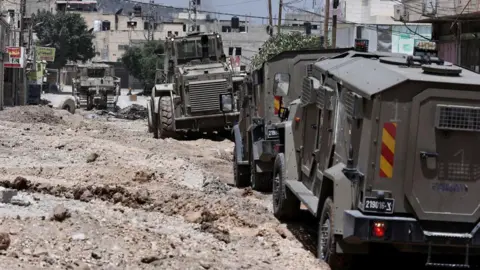 Israeli armoured vehicles drive over a road dug up by a bulldozers in Jenin, in the occupied West Bank (21 May 2024)