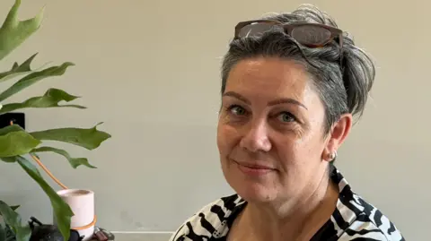 Wendy Bird has short hair with sunglasses on her head. She is wearing a black and white striped T-shirt.
