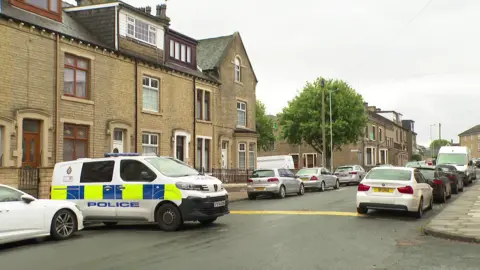 A police van is parked across a street in Bradford which has terraced houses on each side.