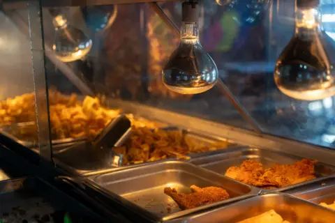 Fritz Pinnow fried fried pork, chicken and banana are displayed in trays under a heat lamp in comayagua